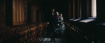 Movie still from “The Invisible Woman” (2013), directed by Ralph Fiennes – A man and two women are standing in front of rows of chairs; Wide shot, High angle