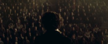 Movie still from “The Invisible Woman” (2013), directed by Ralph Fiennes – A person is standing in front of an audience; Medium shot, Over the shoulder angle