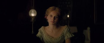 Movie still from “The Invisible Woman” (2013), directed by Ralph Fiennes – A woman in a white dress sitting in front of a lamp; Close Up shot, Over the shoulder angle