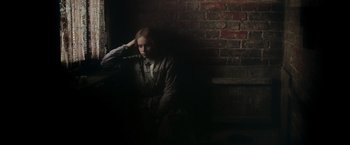 Movie still from “The Invisible Woman” (2013), directed by Ralph Fiennes – A woman sitting in a dark room next to a brick wall; Medium shot, High angle