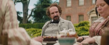 Movie still from “The Invisible Woman” (2013), directed by Ralph Fiennes – A man sitting at a table in front of a cake; Medium shot, Over the shoulder angle
