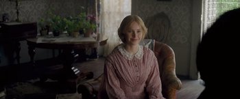 Movie still from “The Invisible Woman” (2013), directed by Ralph Fiennes – A woman in a pink dress sitting in a chair in front of a window; Medium shot, Over the shoulder angle