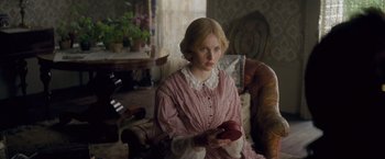 Movie still from “The Invisible Woman” (2013), directed by Ralph Fiennes – A woman in a pink dress holding an apple in a living room; Medium shot, Over the shoulder angle