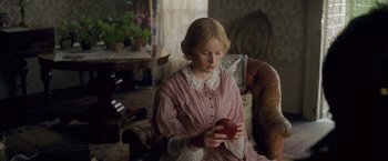 Movie still from “The Invisible Woman” (2013), directed by Ralph Fiennes – A young woman holding an apple while sitting on a couch; Medium shot, Over the shoulder angle