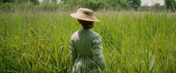 Movie still from “The Invisible Woman” (2013), directed by Ralph Fiennes – A woman wearing a hat standing in tall grass; Medium shot, High angle