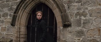 Movie still from “The Invisible Woman” (2013), directed by Ralph Fiennes – A woman in a long black coat standing in front of a door; Medium shot, Low angle
