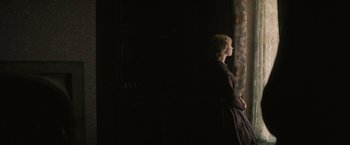 Movie still from “The Invisible Woman” (2013), directed by Ralph Fiennes – A woman standing in front of a curtain in a dark room; Medium shot, Over the shoulder angle