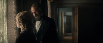 Movie still from “The Invisible Woman” (2013), directed by Ralph Fiennes – A man in a suit and tie standing next to a door way; Medium shot, Over the shoulder angle