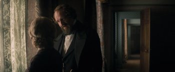 Movie still from “The Invisible Woman” (2013), directed by Ralph Fiennes – A man with a beard wearing a suit and tie; Medium shot, Over the shoulder angle