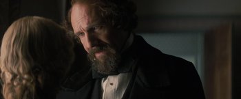 Movie still from “The Invisible Woman” (2013), directed by Ralph Fiennes – A man with a long beard wearing a suit and bow tie; Close Up shot, Over the shoulder angle