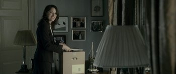 Movie still from “The Iron Lady” (2011), directed by Phyllida Lloyd – A woman standing in front of a box in a living room; Medium shot, Over the shoulder angle