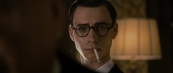 Movie still from “The Iron Lady” (2011), directed by Phyllida Lloyd – A man in a suit and glasses smoking a cigarette; Close Up shot, Over the shoulder angle