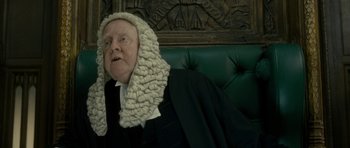 Movie still from “The Iron Lady” (2011), directed by Phyllida Lloyd – An old man wearing a judge's wig sitting on a bench; Close Up shot, Over the shoulder angle