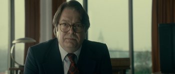 Movie still from “The Iron Lady” (2011), directed by Phyllida Lloyd – A man in a suit and tie sitting in front of a window; Close Up shot, Over the shoulder angle