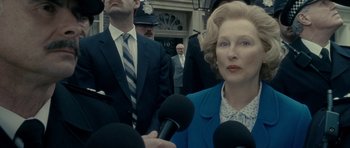 Movie still from “The Iron Lady” (2011), directed by Phyllida Lloyd – A woman is being interviewed by reporters outside a building; Close Up shot, Over the shoulder angle
