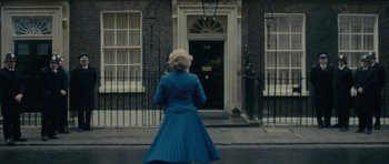 Movie still from “The Iron Lady” (2011), directed by Phyllida Lloyd – A woman in a long blue dress standing in front of a door; Wide shot, High angle