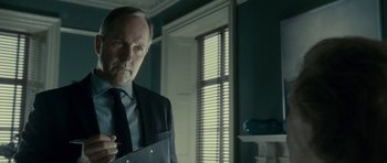 Movie still from “The Iron Lady” (2011), directed by Phyllida Lloyd – A man in a suit and tie in a room; Close Up shot, Low angle