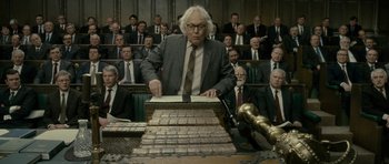 Movie still from “The Iron Lady” (2011), directed by Phyllida Lloyd – An old man in a suit and tie in front of a bunch of men; Medium shot, Low angle