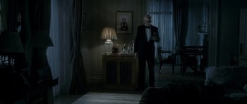 Movie still from “The Iron Lady” (2011), directed by Phyllida Lloyd – An older man in a suit and tie looking at his cell phone; Wide shot, Low angle