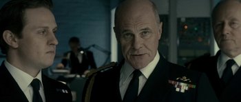 Movie still from “The Iron Lady” (2011), directed by Phyllida Lloyd – A man in a suit and tie standing in front of a camera; Close Up shot, Low angle