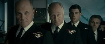 Movie still from “The Iron Lady” (2011), directed by Phyllida Lloyd – A man in a suit and tie standing next to two other men; Medium shot, Low angle