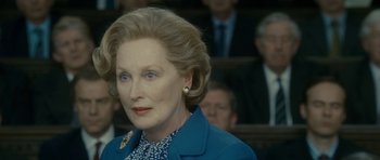 Movie still from “The Iron Lady” (2011), directed by Phyllida Lloyd – An older woman in a blue jacket looks at the camera; Close Up shot, Over the shoulder angle