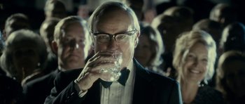 Movie still from “The Iron Lady” (2011), directed by Phyllida Lloyd – A man in a tuxedo drinking a glass of water; Close Up shot, Over the shoulder angle