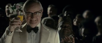 Movie still from “The Iron Lady” (2011), directed by Phyllida Lloyd – An older man wearing a white suit and a bow tie; Close Up shot, Over the shoulder angle