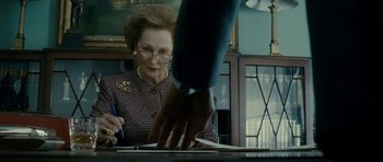 Movie still from “The Iron Lady” (2011), directed by Phyllida Lloyd – An older woman sitting at a table with a hand on a desk; Close Up shot, Over the shoulder angle