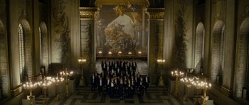 Movie still from “The Iron Lady” (2011), directed by Phyllida Lloyd – A group of people in suits and ties in front of a large painting; Extreme Wide shot, High angle