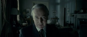 Movie still from “The Iron Lady” (2011), directed by Phyllida Lloyd – An older man wearing a suit and tie in a living room; Close Up shot, Low angle