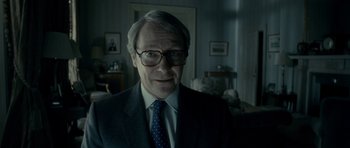 Movie still from “The Iron Lady” (2011), directed by Phyllida Lloyd – An older man wearing a suit and tie in a living room; Close Up shot, Over the shoulder angle