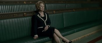 Movie still from “The Iron Lady” (2011), directed by Phyllida Lloyd – An older woman sitting on a bench in a room; Medium shot, Low angle
