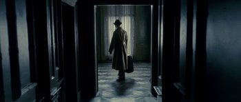 Movie still from “The Iron Lady” (2011), directed by Phyllida Lloyd – A man in a hat and a trench coat is holding a suitcase; Wide shot, Low angle