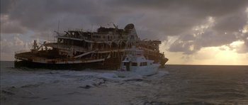 Movie still from “The Island” (1980), directed by Michael Ritchie – A boat is in the water near a large ship; Extreme Wide shot, Low angle