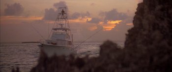 Movie still from “The Island” (1980), directed by Michael Ritchie – A boat in the ocean at sunset with clouds in the background; Extreme Wide shot, Low angle