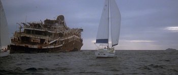 Movie still from “The Island” (1980), directed by Michael Ritchie – A boat in the water next to an old ship; Extreme Wide shot, Low angle