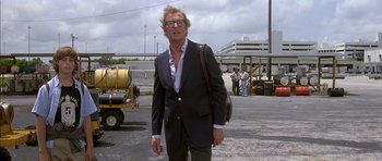 Movie still from “The Island” (1980), directed by Michael Ritchie – A man in a suit and glasses walking in a parking lot; Medium shot, Low angle