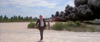 Movie still from “The Island” (1980), directed by Michael Ritchie – A man in a suit walking in front of an airplane on fire; Wide shot, Low angle