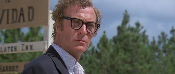 Movie still from “The Island” (1980), directed by Michael Ritchie – A person wearing glasses and a suit; Close Up shot, Low angle