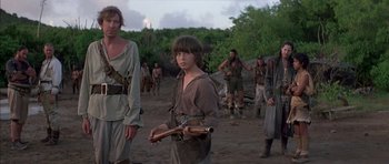 Movie still from “The Island” (1980), directed by Michael Ritchie – A group of people standing in the dirt; Medium shot, Over the shoulder angle