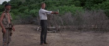 Movie still from “The Island” (1980), directed by Michael Ritchie – A man in a white shirt and black pants throwing a frisbee in the dirt; Medium shot, Low angle