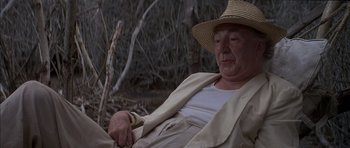 Movie still from “The Island” (1980), directed by Michael Ritchie – An older man wearing a straw hat is sitting in the woods; Medium shot, Low angle