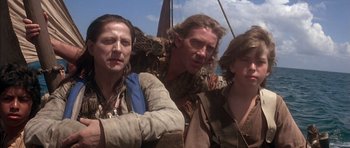 Movie still from “The Island” (1980), directed by Michael Ritchie – A group of people standing next to each other on top of a boat; Medium shot, Over the shoulder angle