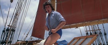 Movie still from “The Island” (1980), directed by Michael Ritchie – A man in blue shorts and a blue shirt holding onto a rope; Medium shot, Low angle