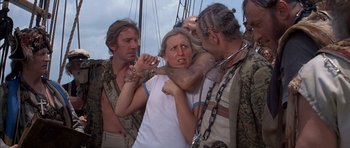 Movie still from “The Island” (1980), directed by Michael Ritchie – A group of people standing around a woman with her mouth open; Medium shot, Over the shoulder angle