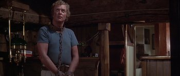 Movie still from “The Island” (1980), directed by Michael Ritchie – A man in chains standing in a room; Medium shot, Low angle