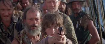 Movie still from “The Island” (1980), directed by Michael Ritchie – A group of people standing around a young boy holding a gun; Close Up shot, Over the shoulder angle