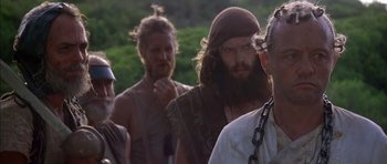 Movie still from “The Island” (1980), directed by Michael Ritchie – A group of men standing next to each other on a field; Close Up shot, Over the shoulder angle
