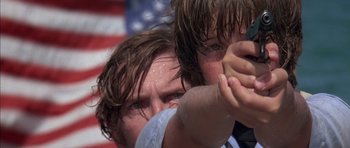 Movie still from “The Island” (1980), directed by Michael Ritchie – Two men with wet hair and wet shirts are fighting in front of an american flag; Close Up shot, Low angle